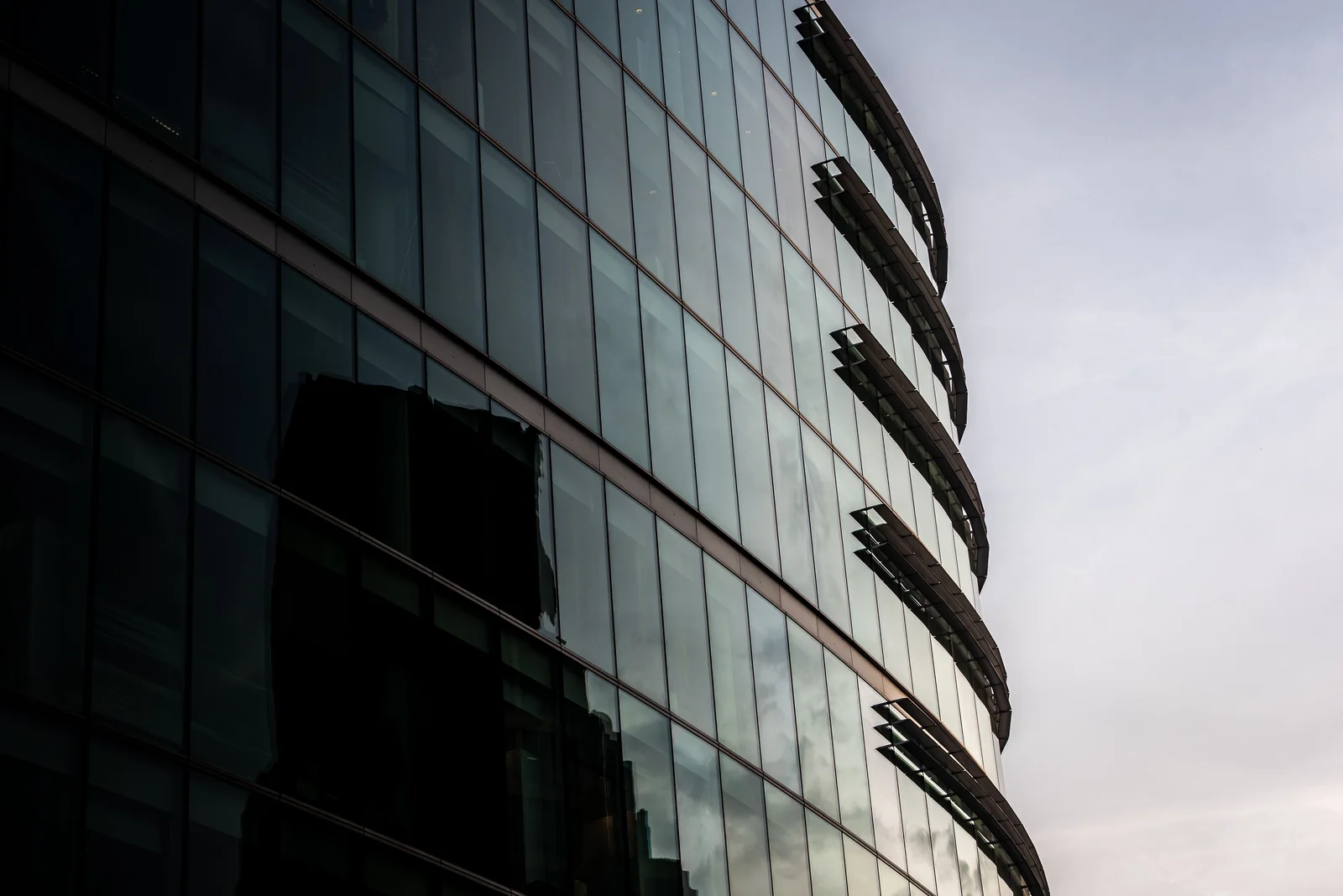Curved glass office facade reflecting nearby buildings beneath an overcast sky.