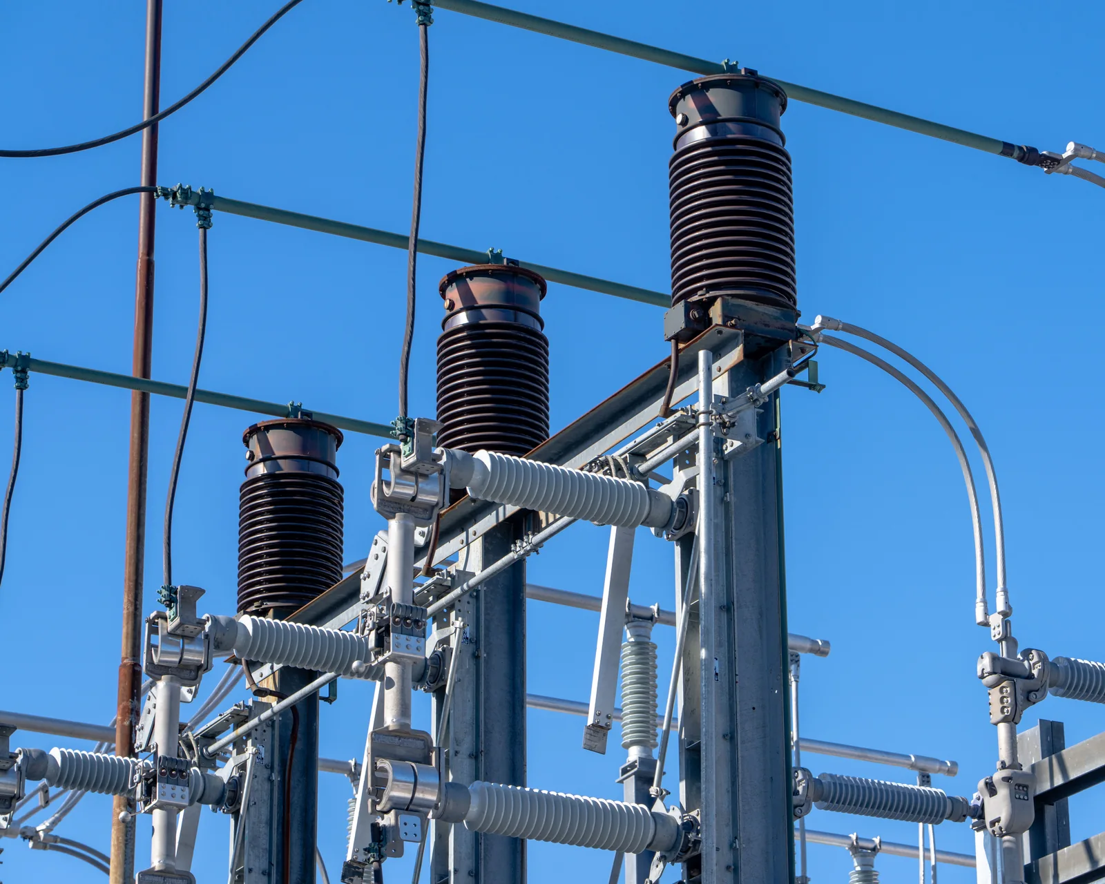 Insulators, conductors, and steel supports at an electrical substation beneath a clear blue sky.