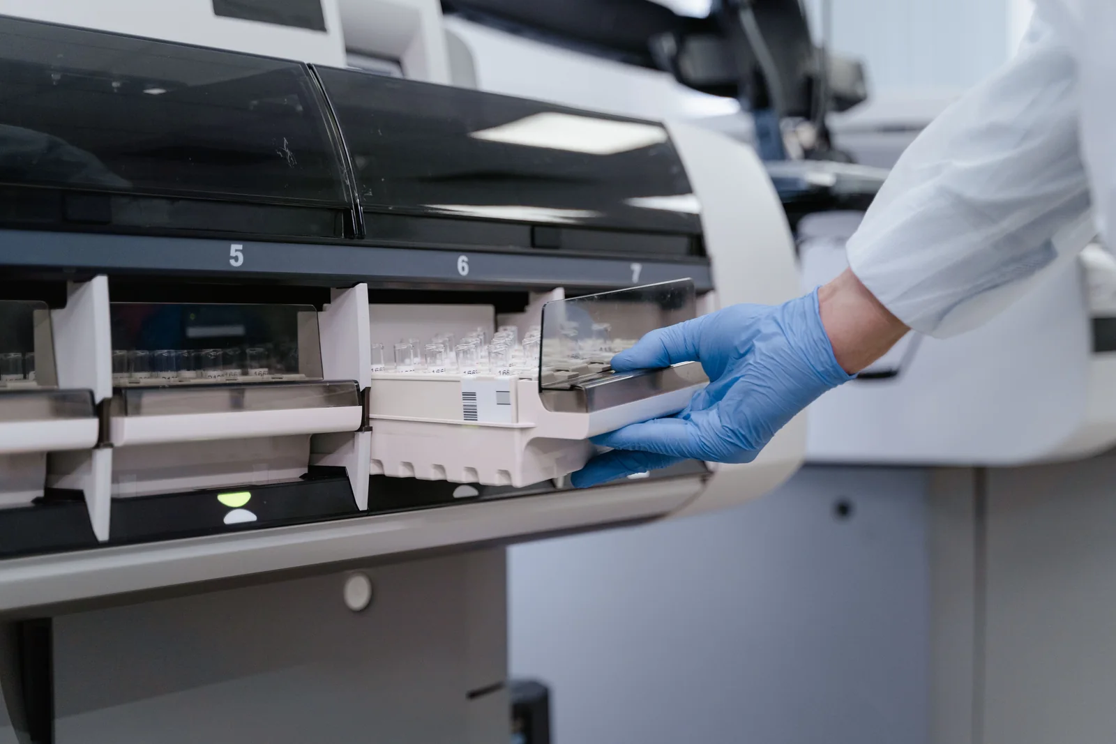 A blue-gloved hand loading sample trays into laboratory analysis equipment.