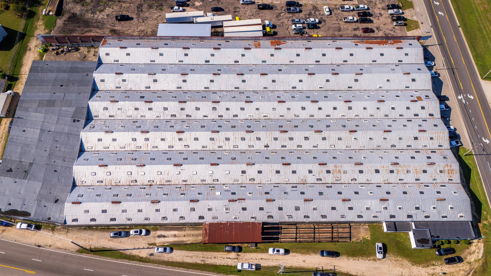 Aerial view of a large warehouse with trailers, parked vehicles, and surrounding roads.