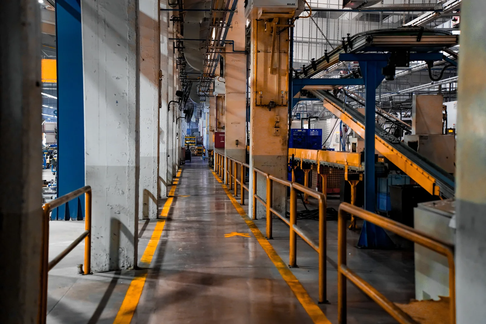 Factory walkway beside conveyor machinery, steel columns, and safety railings.
